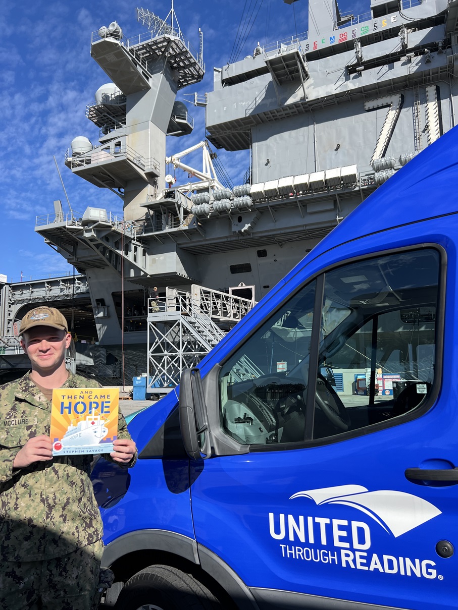 Service member holds book in front of United Through Reading Mobile Story Station