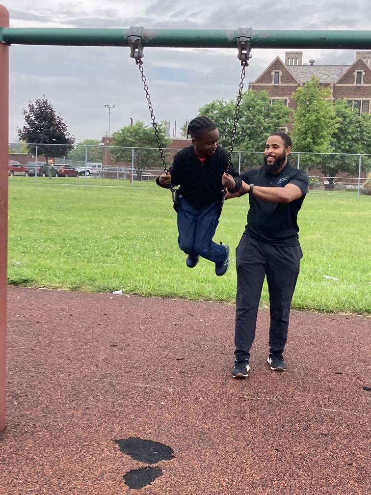 FR1ENDS of the CH1LDREN Detroit mentor Zeke pushes mentee on swing at playground