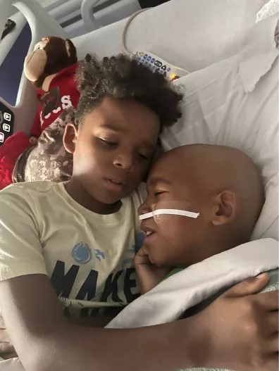 Sibling lies next to child cancer patient in hospital bed