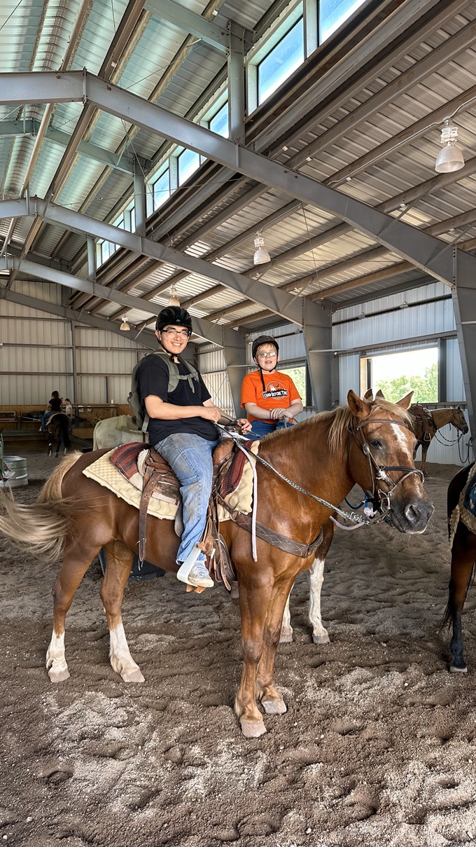 Arizona Camp Sunrise and Sidekicks Southwest Kids Cancer Foundation two smiling, helmeted boys on horseback in barn